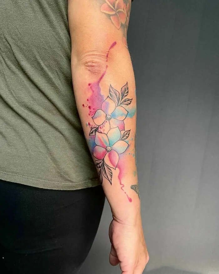 Colorful watercolor tattoo of flowers on a forearm.