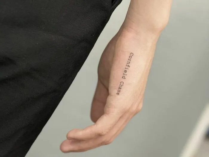 Word tattoo reading "Cornfield Chase" on a person's forearm.
