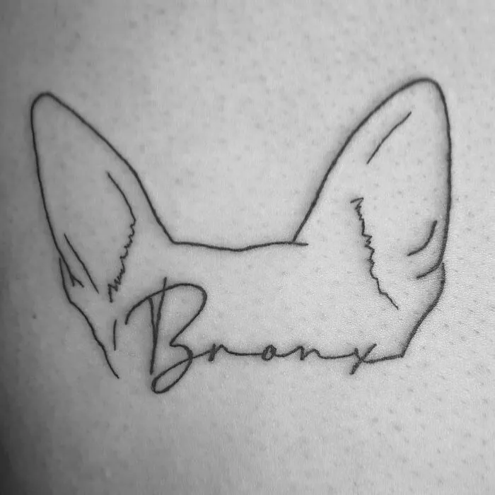 Pet tattoo of dog's ears with "Bronx" underneath, symbolizing the bond between humans and their pets.