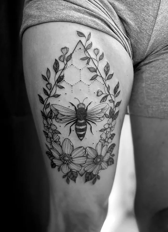Bee tattoo with floral elements on a thigh, celebrating the animal kingdom.