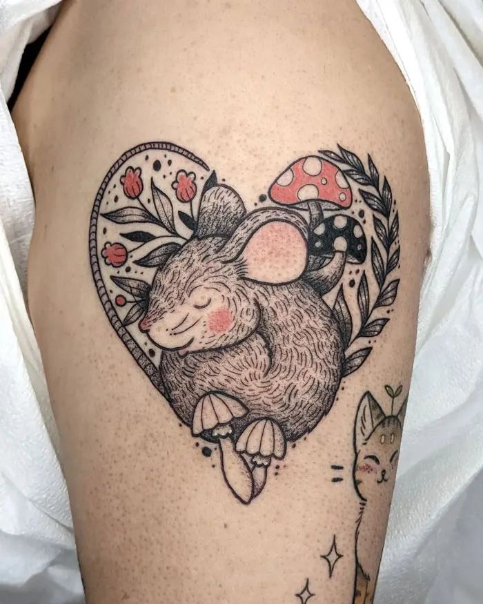 A simple and realistic animal tattoo of a mouse inside a heart shape with floral accents and mushrooms.