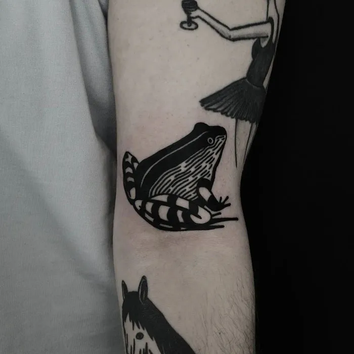 Black ink frog tattoo on arm, showcasing simplicity and realism in animal art.