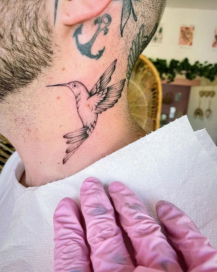 Hummingbird tattoo on a man’s neck, showcasing animal tattoos with an anchor tattoo above.