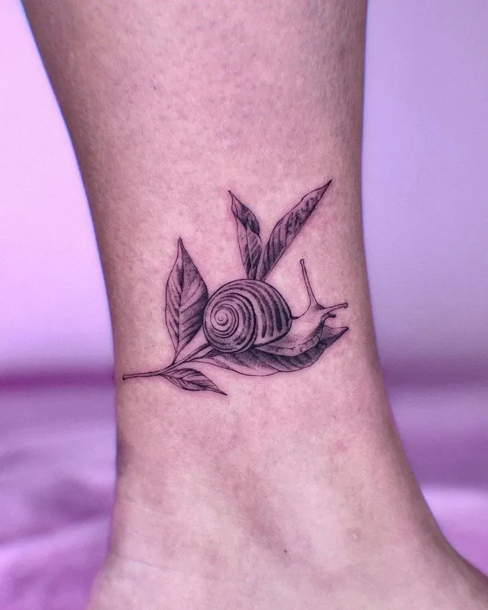 Snail tattoo on ankle with leaves, celebrating the animal kingdom.