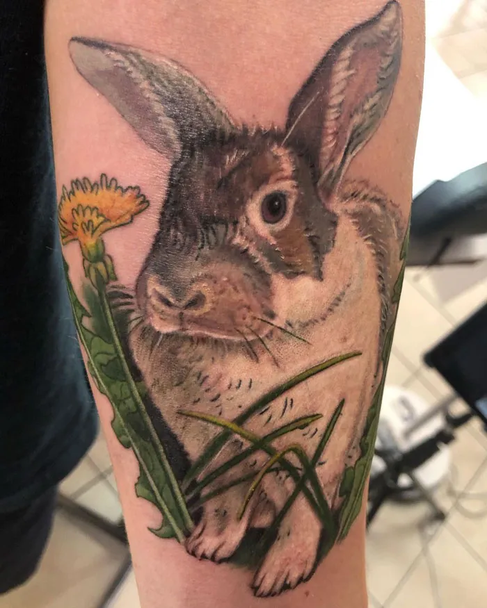 Animal tattoo featuring a realistic rabbit with a dandelion, celebrating the animal kingdom on a forearm.