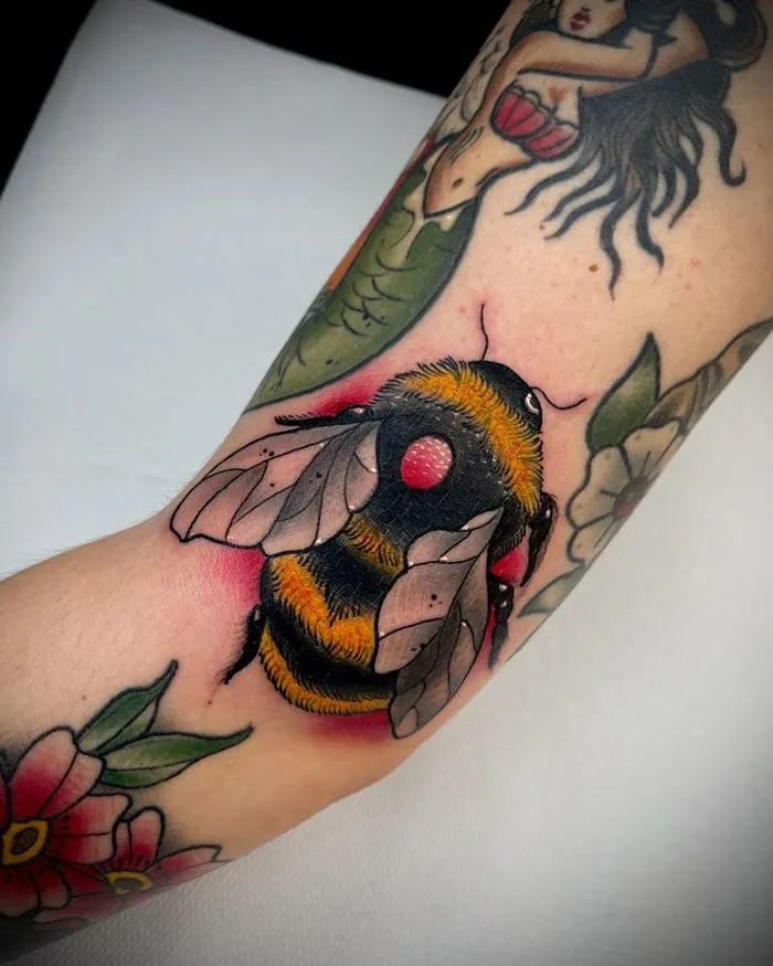 Vibrant bee tattoo with floral and mermaid designs, celebrating the animal kingdom on a forearm.