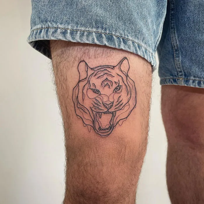 Animal tattoo of a realistic tiger face on a person's thigh, showcasing simplicity.