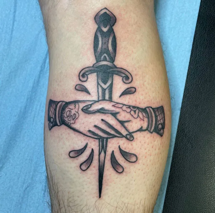 Lower leg tattoo of two shaking hands over a dagger with intricate details.