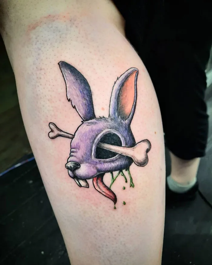 Lower leg tattoo featuring a cartoonish rabbit skull with a bone and green slime detail.