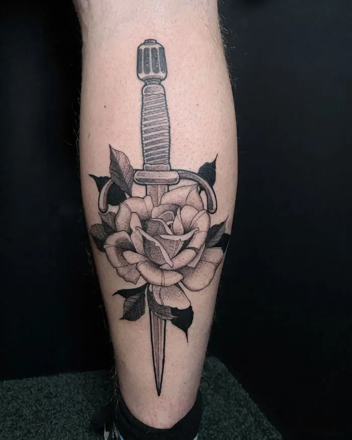 Lower leg tattoo of a dagger through a rose, showcasing detailed black ink design.