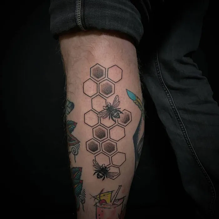 Lower leg tattoos featuring bees and honeycomb pattern on calf.