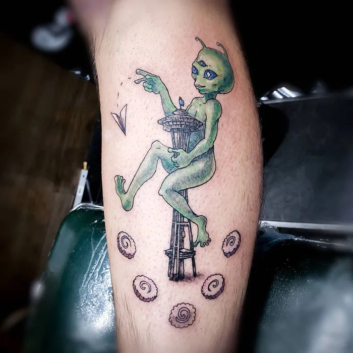 Alien tattoo design on calf featuring the Space Needle and a paper airplane.