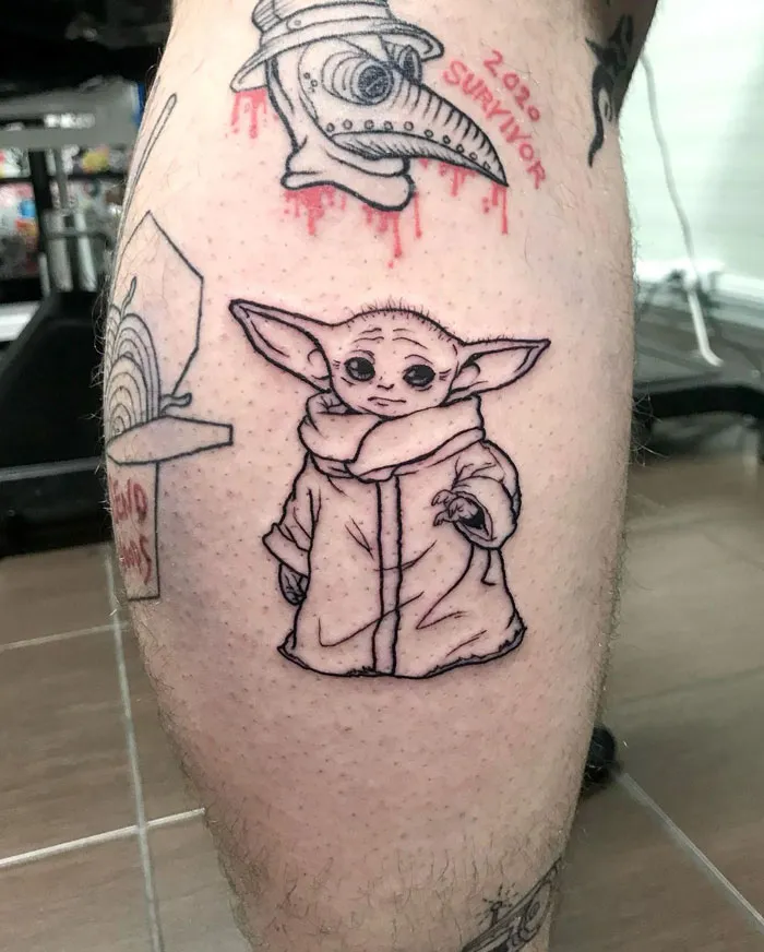 Lower leg tattoos featuring a hooded character and plague doctor mask symbolize creativity and pop culture influences.