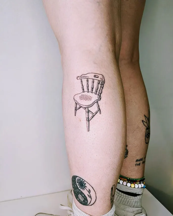 Unique calf tattoo of a chair design on a person's leg, surrounded by other small tattoos.