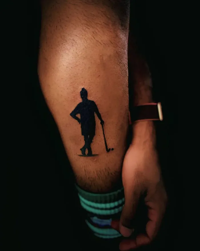 Silhouette tattoo on a lower leg featuring a golfer with a club.