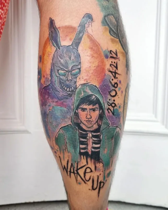 Lower leg tattoo featuring a hooded figure and sinister rabbit with “Wake Up” text.
