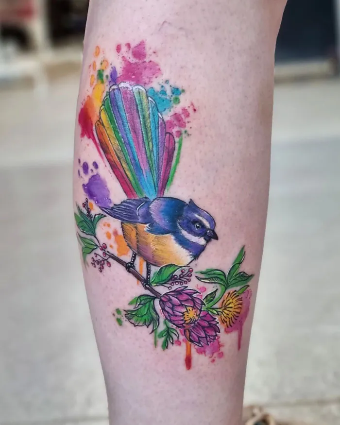 Colorful bird and floral design on calf tattoo, showcasing unique calf tattoo ideas with vibrant rainbow tail and blossoms.