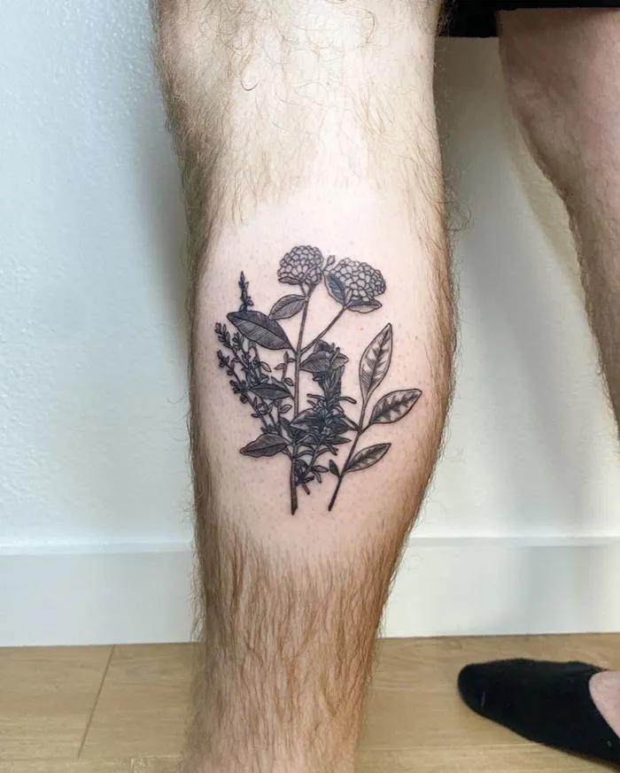 Black floral design on a lower leg tattoo, showcasing intricate botanical details.
