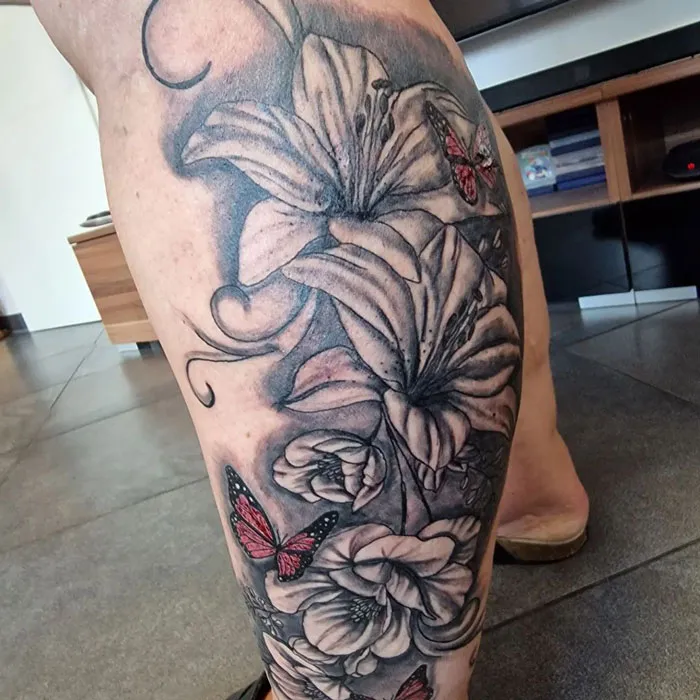 Floral calf tattoo featuring lilies and red butterflies, showcasing cool tattoo design ideas.