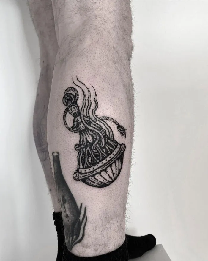 Ornate black calf tattoo featuring a detailed vase design against a neutral background.