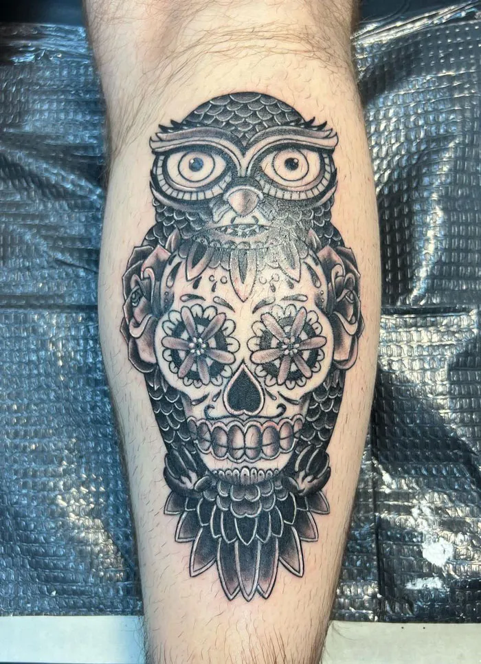 Owl and sugar skull lower leg tattoo with floral elements.