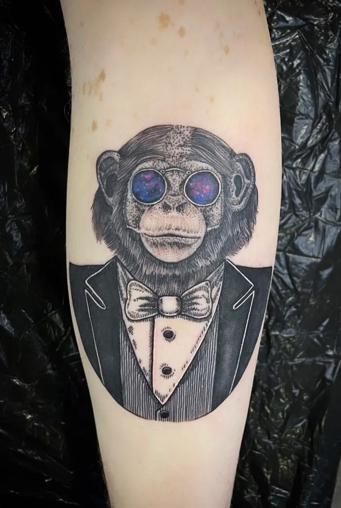 Calf tattoo of a chimpanzee in a tuxedo with galaxy glasses, showcasing unique and cool design ideas.