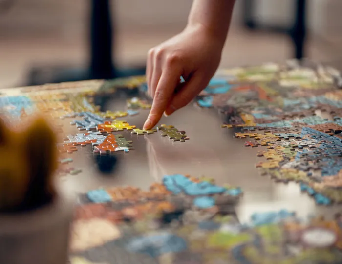 A person assembling a colorful puzzle on a glass table at home, focusing on fun activities to avoid boredom.