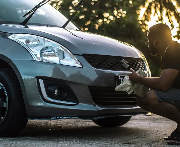 Man washing a car with a cloth, focusing on the front grille in sunlight, enjoying a fun activity to avoid boredom at home.
