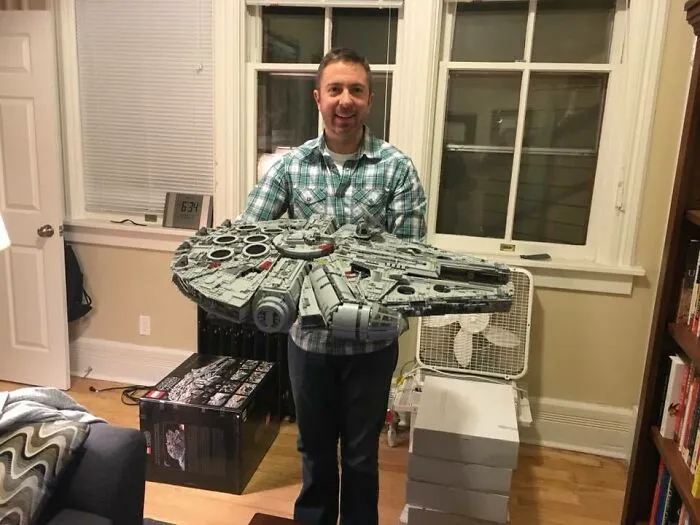 Man holding an incredible LEGO build of the Millennium Falcon, showcasing detailed and artistic LEGO craftsmanship indoors.