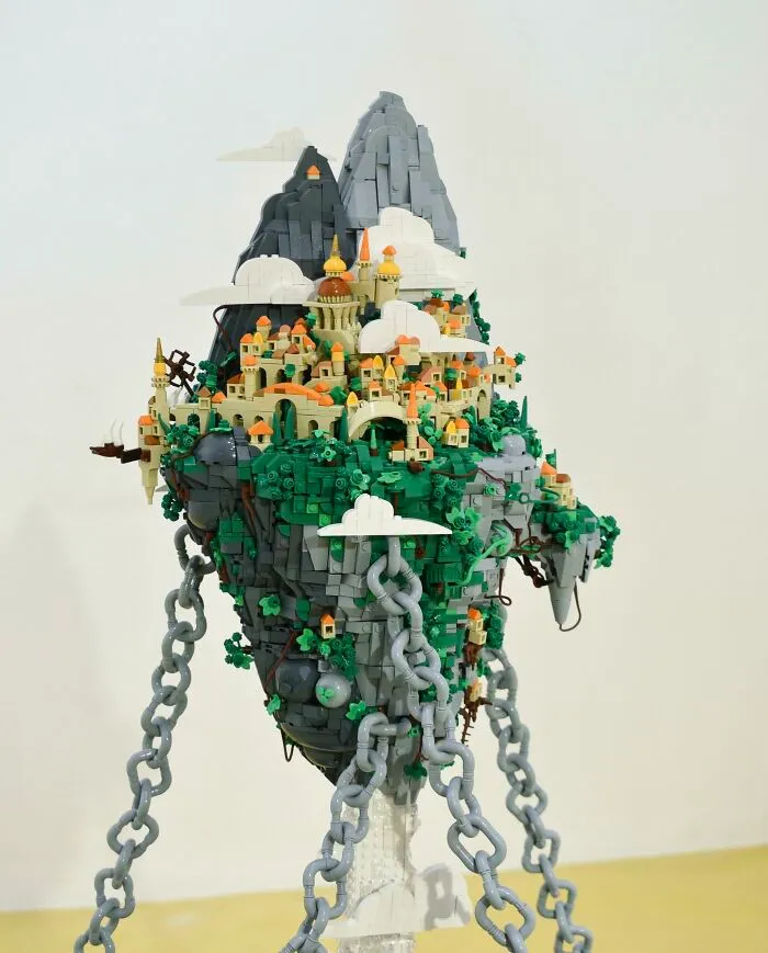 Intricate LEGO build of a floating island city with detailed buildings, greenery, and large chains anchoring it in place.