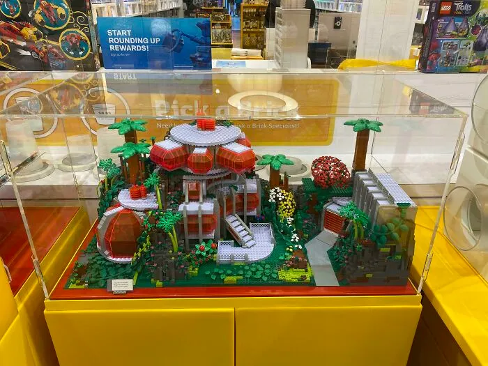 Intricate LEGO builds displayed in a glass case featuring a detailed futuristic house with surrounding trees and plants.