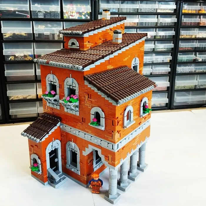 Intricate orange and brown LEGO build of a multi-story building with windows, columns, and flower boxes in front of storage bins.