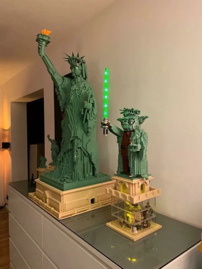 LEGO builds of the Statue of Liberty and Yoda holding a glowing green lightsaber displayed on a glass surface.