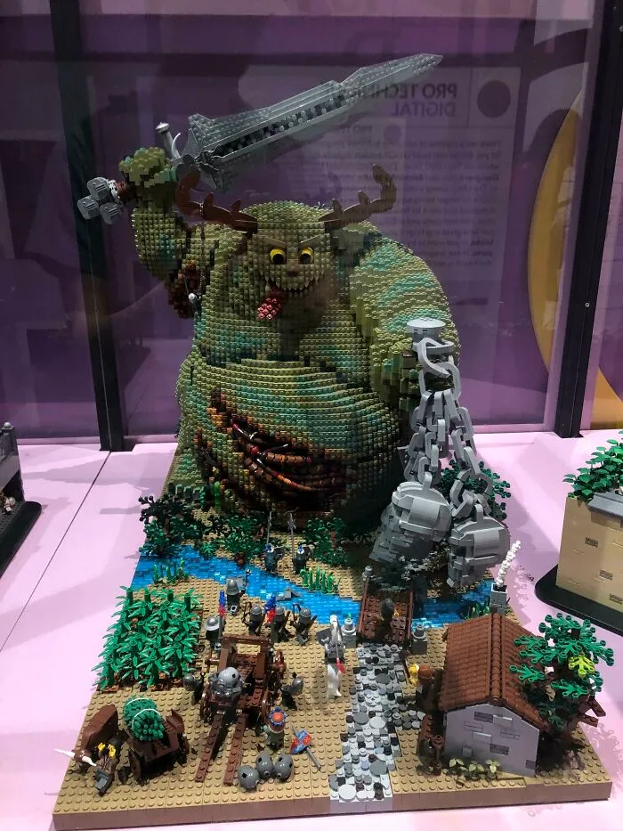 LEGO build of a giant warrior with sword and chain, surrounded by miniature soldiers and village in detailed scene.
