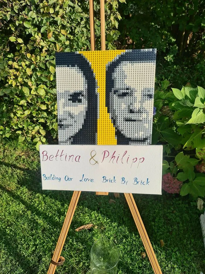 LEGO artwork of two faces on an easel with a sign about building love brick by brick in a garden setting.