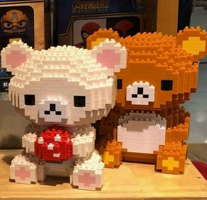 Two incredible LEGO builds of bears, one white holding a red object and one brown, displayed on a wooden surface.