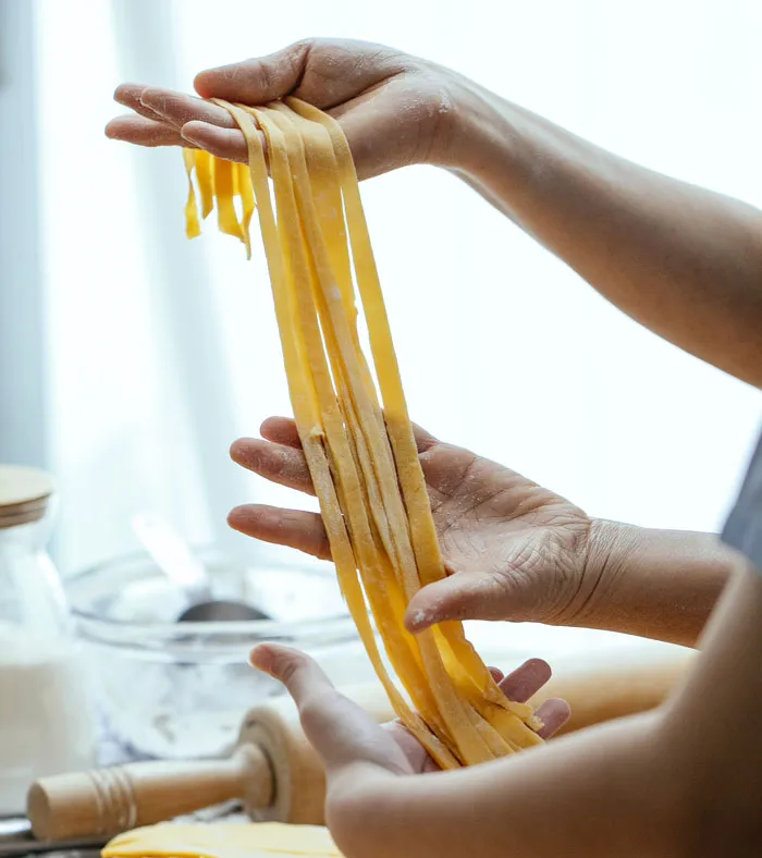 Hands holding freshly made pasta at home, showcasing a fun activity to avoid boredom.