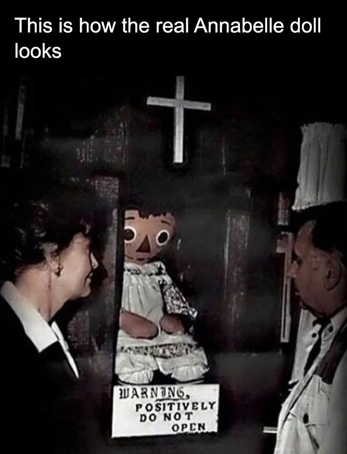 Real Annabelle doll displayed in a case with warning sign, viewed by two people, part of creepy facts and pictures collection.