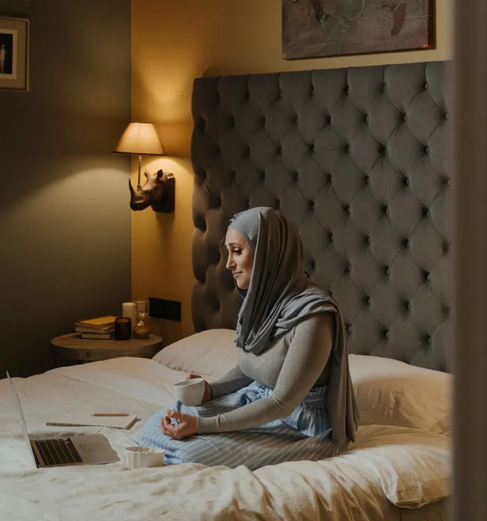 Woman sitting on bed with a laptop and coffee, enjoying fun things to do at home.
