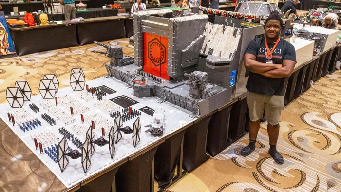 Man standing next to an intricate Star Wars LEGO build showcasing incredible LEGO art at a convention display.