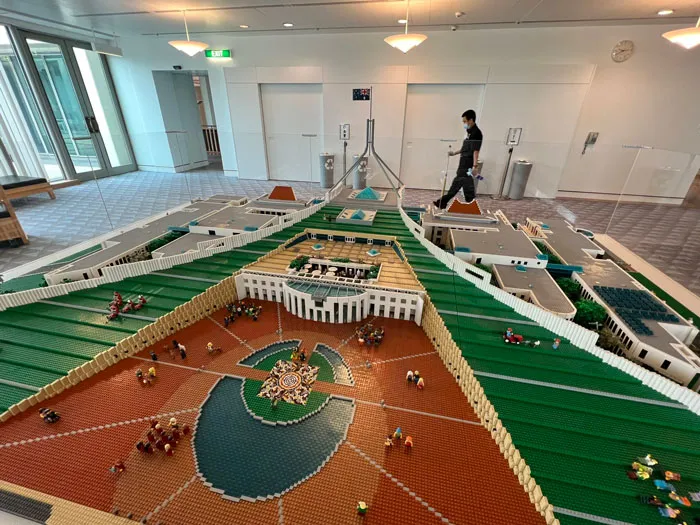 Detailed LEGO builds showcasing an intricate architectural model with miniature figures and green landscaping in an indoor setting.