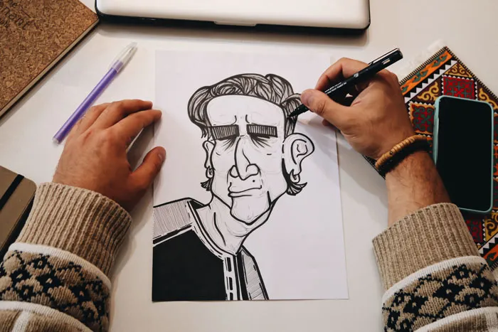 Person drawing a humorous caricature with black pen, featuring bold lines, as part of creative drawing prompts.