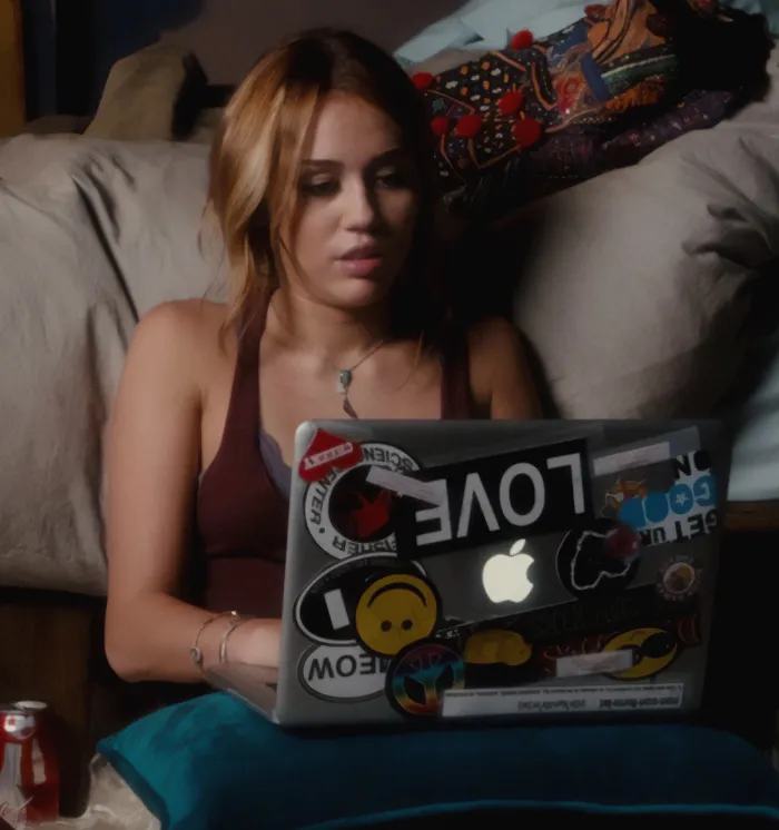 Young woman using a laptop covered in stickers, reflecting signs of a fake friend and a toxic relationship online.