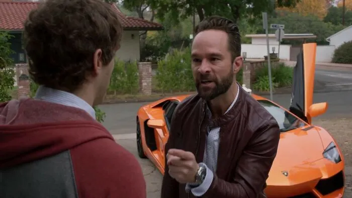 Two men having a tense conversation by an orange sports car, illustrating signs of a fake friend and toxic relationship.