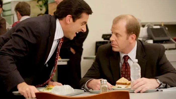 Two men in suits having a tense lunch conversation, illustrating signs of a fake friend and a toxic relationship.
