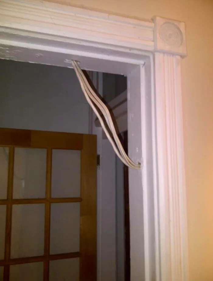 Exposed electrical wires looped above a doorway, ignoring OSHA safety regulations.