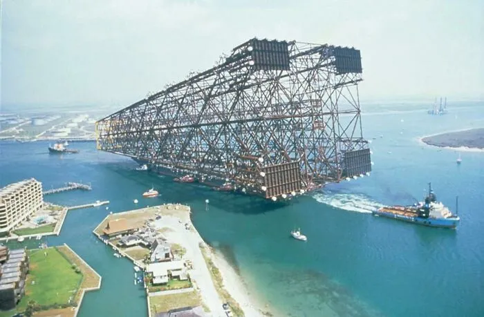Una plataforma petrolera es remolcada al mar. La plataforma eclipsa el lujoso hotel de la izquierda