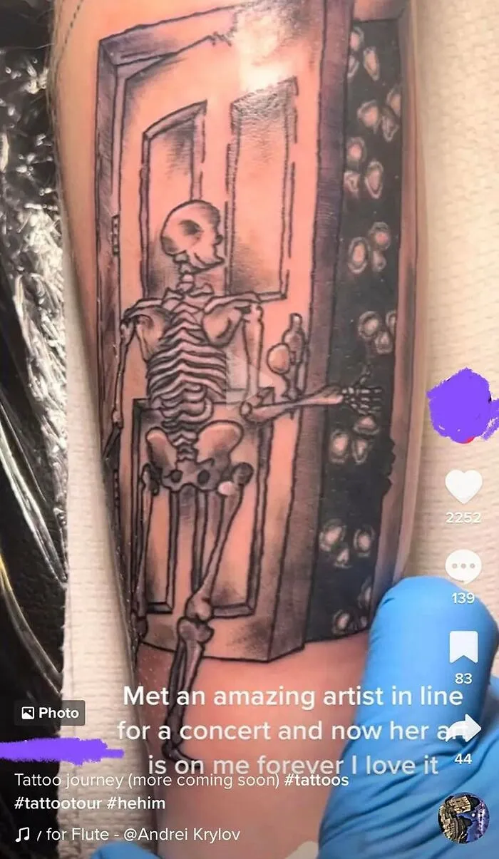 Skeleton tattoo on arm with door and coin design, accompanied by text about a tattoo journey and concert encounter.