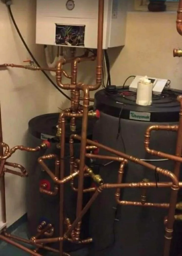 Complex plumbing system with exposed pipes and wires, appearing to disregard OSHA safety regulations.