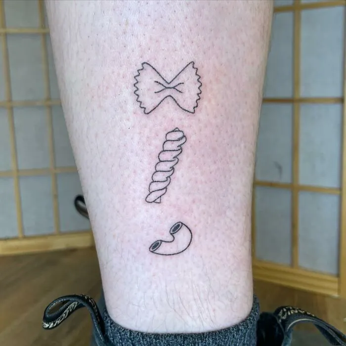 Minimalist tattoo of three pasta shapes on a leg, showcasing an aesthetically pleasing design.